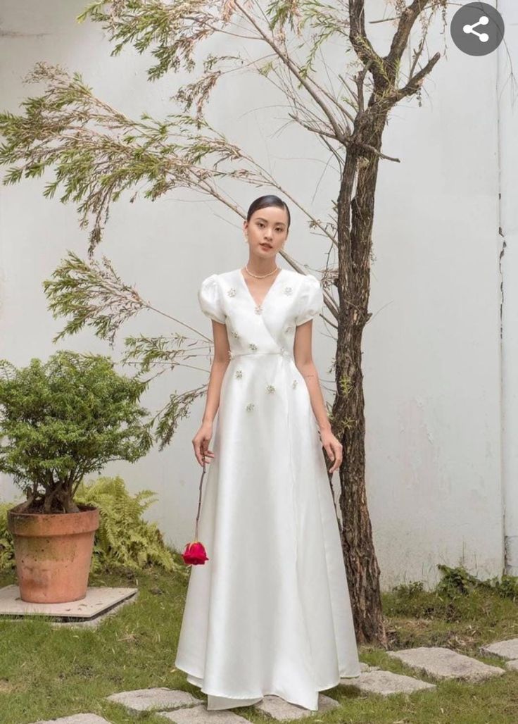 a woman in a white dress standing next to a tree