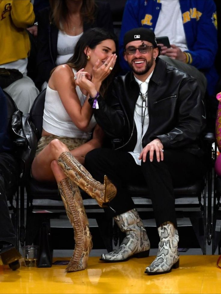 a man and woman sitting next to each other in front of a crowd at a basketball game