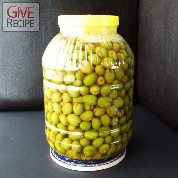 a jar filled with green olives sitting on top of a black table next to a wall