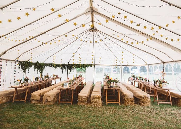 a large tent with hay bales and tables set up for a wedding reception in the grass