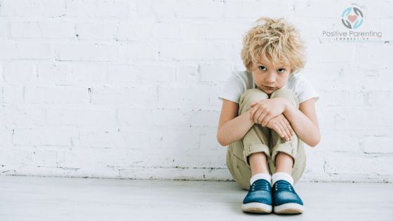 a young boy sitting on the ground with his hands folded in front of his face