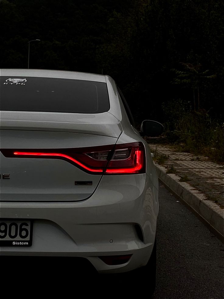 a white car is parked on the side of the road with trees in the background