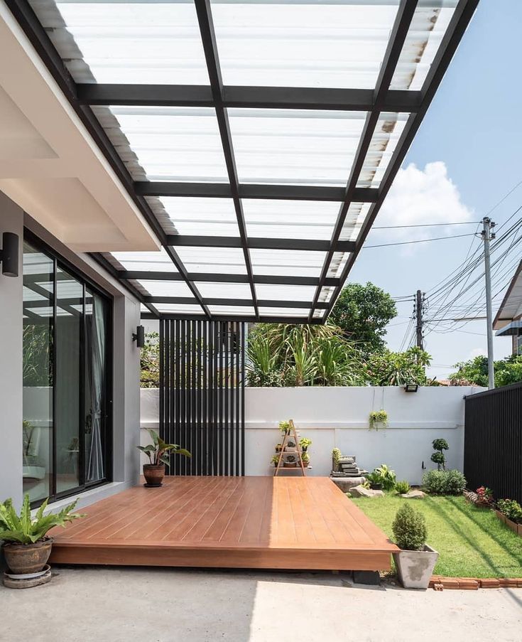 a wooden deck in front of a white house with black metal roofing and glass walls