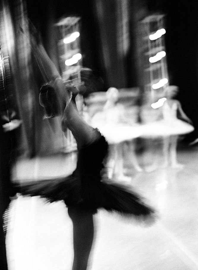 black and white photograph of a woman dancing in a dance studio with blurry lights behind her