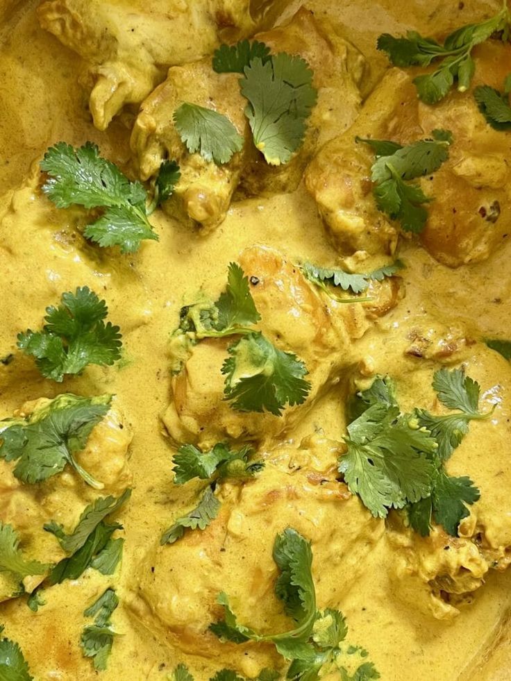 a pan filled with chicken and cilantros covered in yellow sauce, garnished with parsley