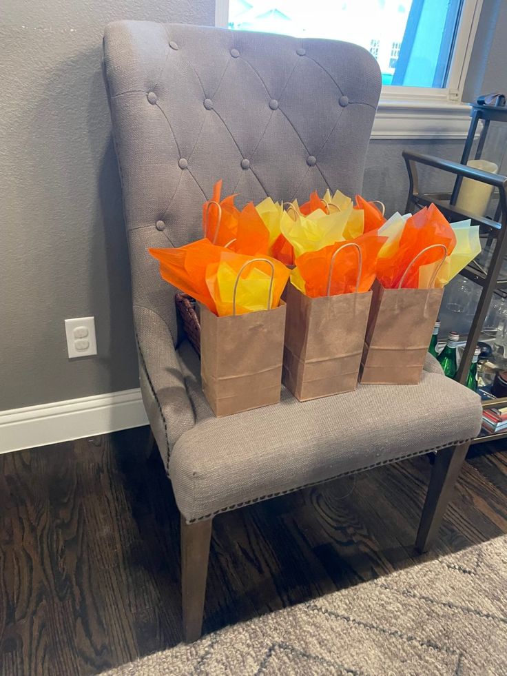 three brown bags with orange and yellow flowers in them sitting on a gray chair next to a window