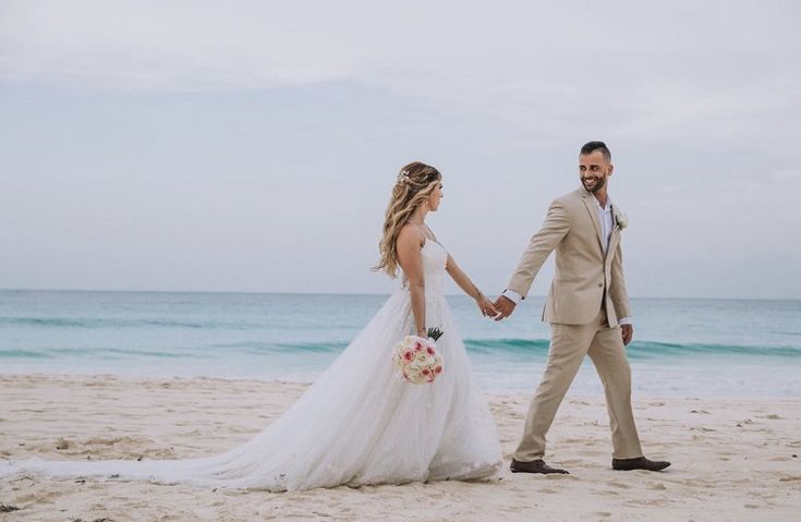 a bride and groom holding hands on the beach