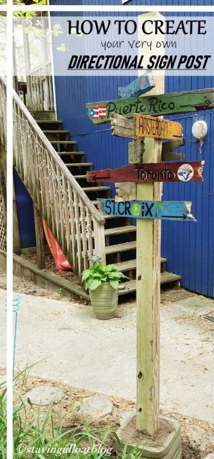 a wooden sign post in front of a blue building with stairs and plants on it