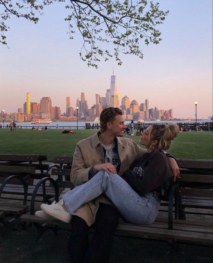 a man and woman sitting on a park bench in front of a cityscape