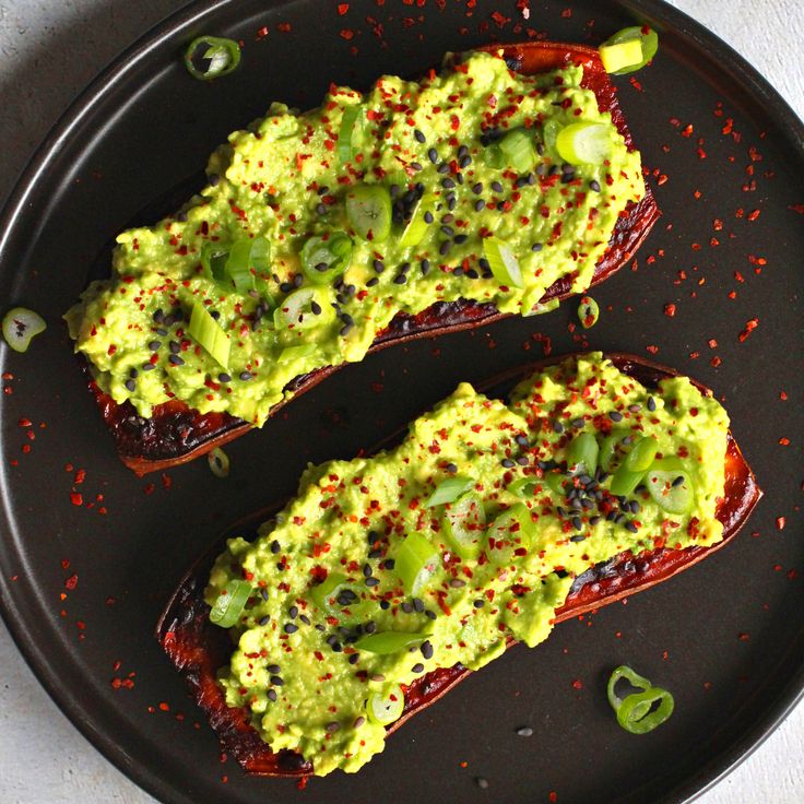 two stuffed peppers covered in guacamole and sprinkles on a black plate