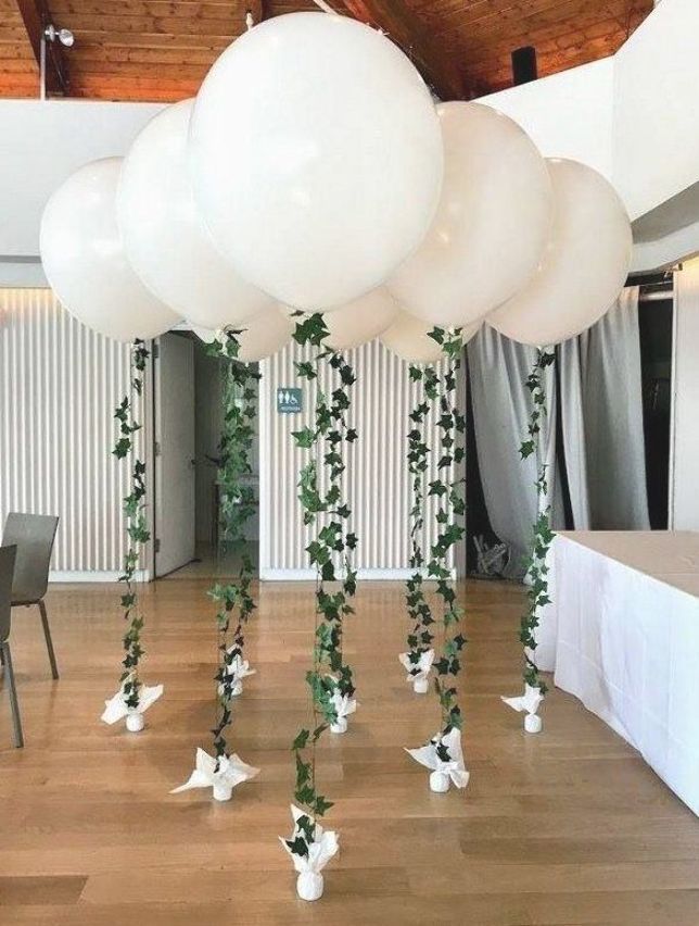 some white balloons are hanging from the ceiling and greenery is on the floor in front of them