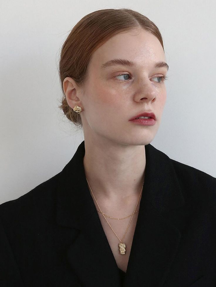 a woman wearing a black jacket and gold necklace, looking off to the side with her eyes closed