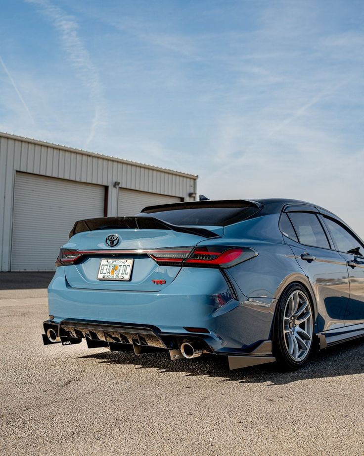 the rear end of a blue car parked in front of a warehouse building on a sunny day