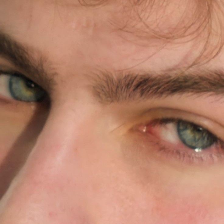 a close up of a man's face with blue eyes and brown hair looking at the camera