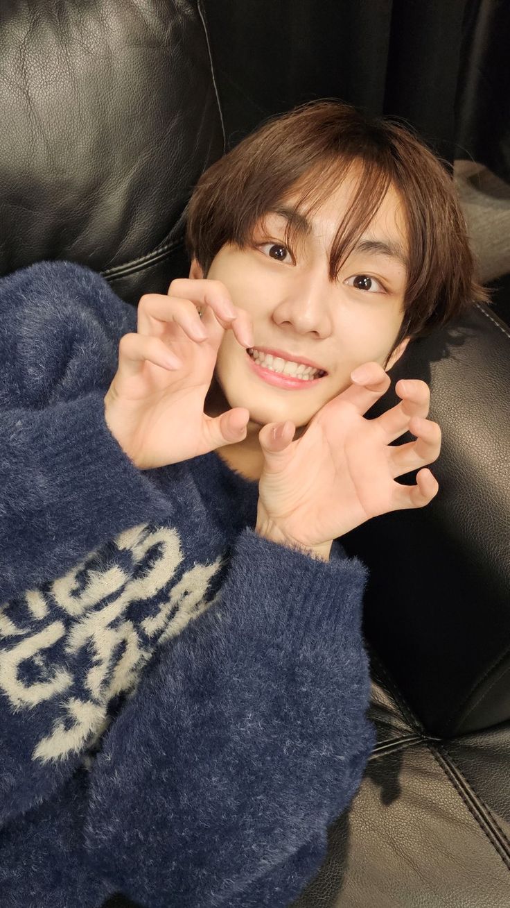 a young man sitting on top of a black leather couch holding his hands in the air