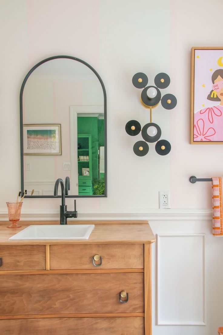 a bathroom with a sink, mirror and art hanging on the wall above it's vanity