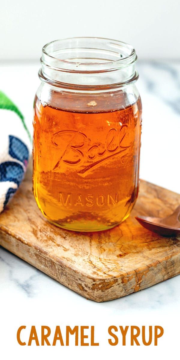 a mason jar filled with caramel syrup on top of a cutting board next to a spoon