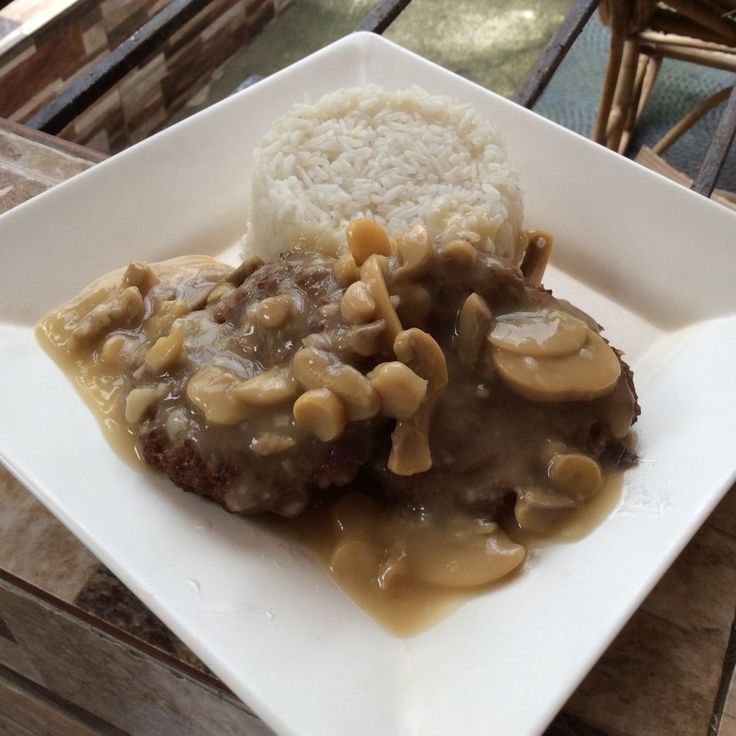 a white plate topped with meat covered in gravy and mushrooms next to rice