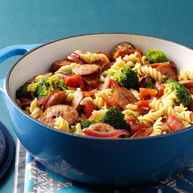 pasta with sausage, broccoli and tomatoes in a blue pot on a table