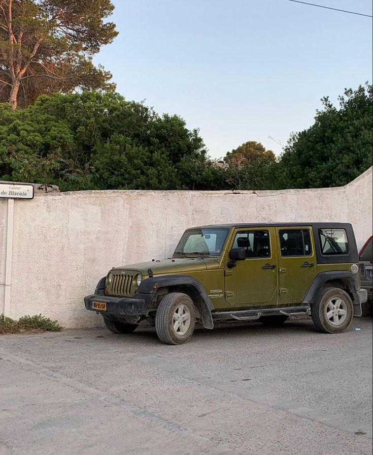 two jeeps parked next to each other in front of a white wall and trees