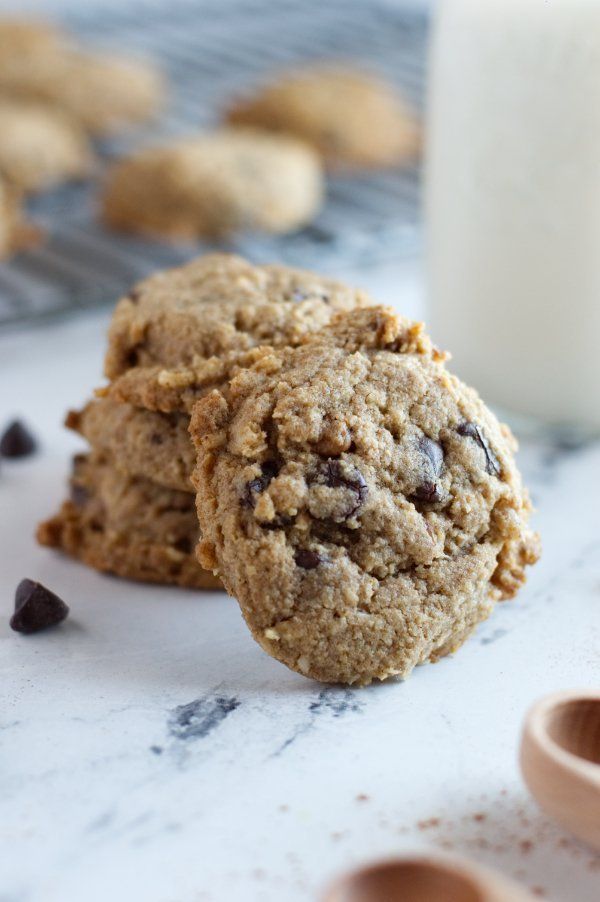 two oatmeal chocolate chip cookies next to a glass of milk on a counter