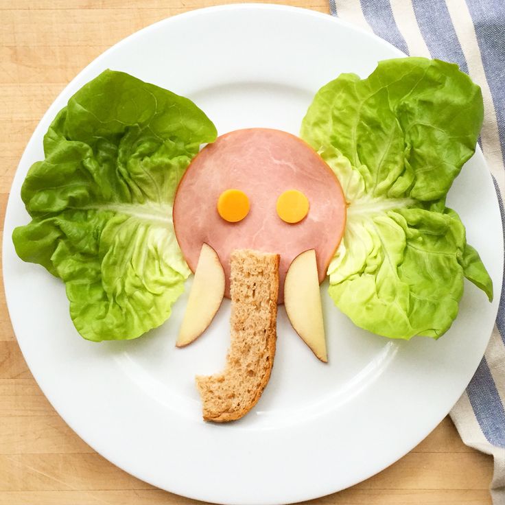 a white plate topped with lettuce and an elephant face made out of meat