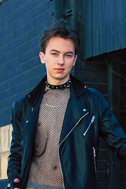 a young man wearing a black leather jacket and tie standing in front of a building