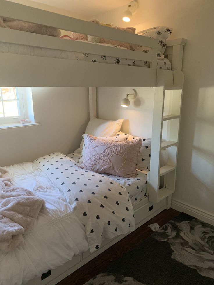 a white bunk bed sitting next to a window with pink pillows on top of it