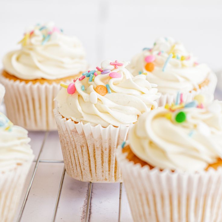 cupcakes with white frosting and sprinkles on a cooling rack