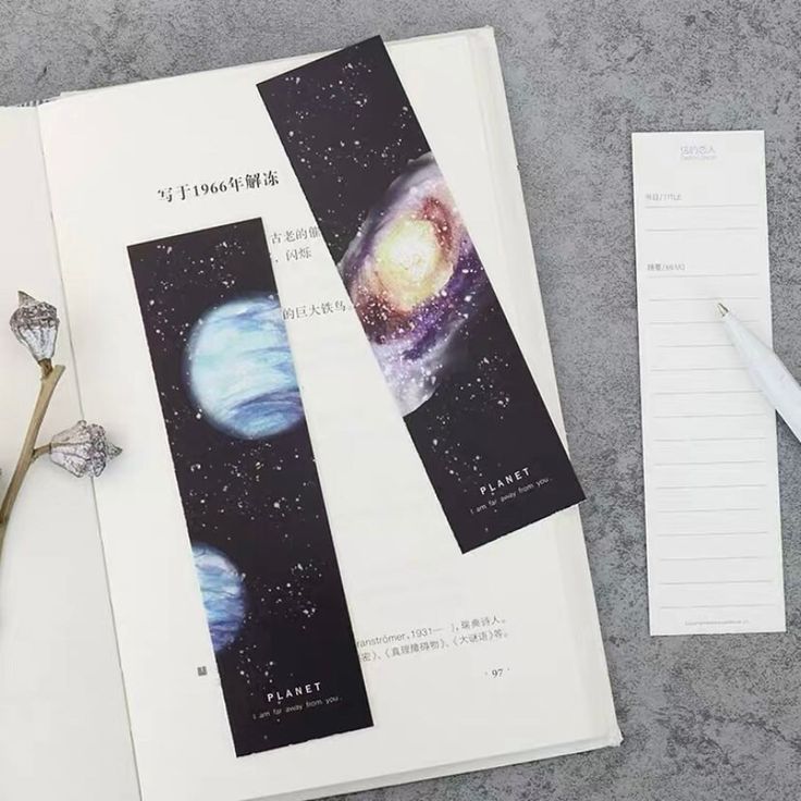 an open book with space images on the pages and writing paper next to it, along with a pair of scissors