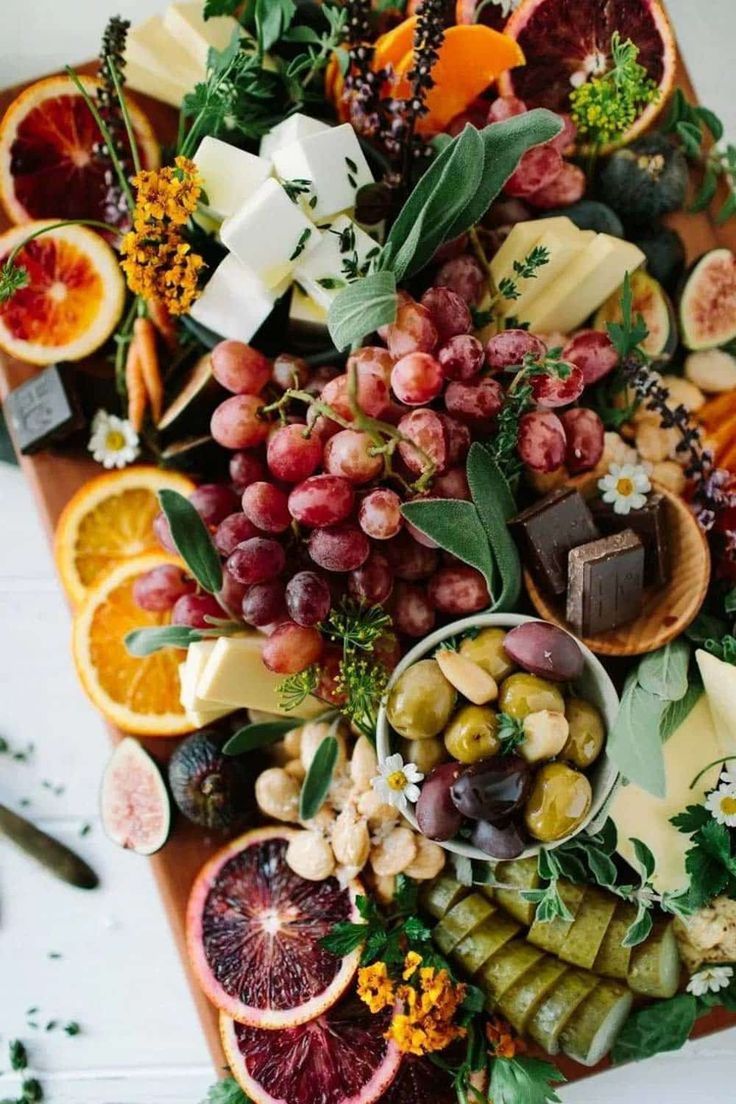 an assortment of fruits and cheeses on a wooden platter with leaves, oranges, grapes, walnuts