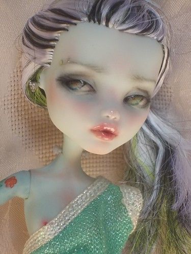 a close up of a doll with long hair and green dress on it's head