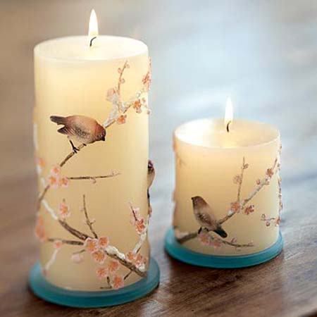 two candles sitting on top of a wooden table with birds painted on the candle holders