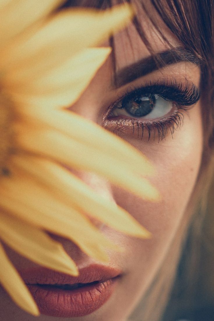 a woman's face with sunflowers in front of her and the bottom half of her eye