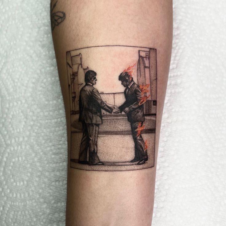 two men shaking hands in front of a fire scene tattoo on the left forearm and right arm