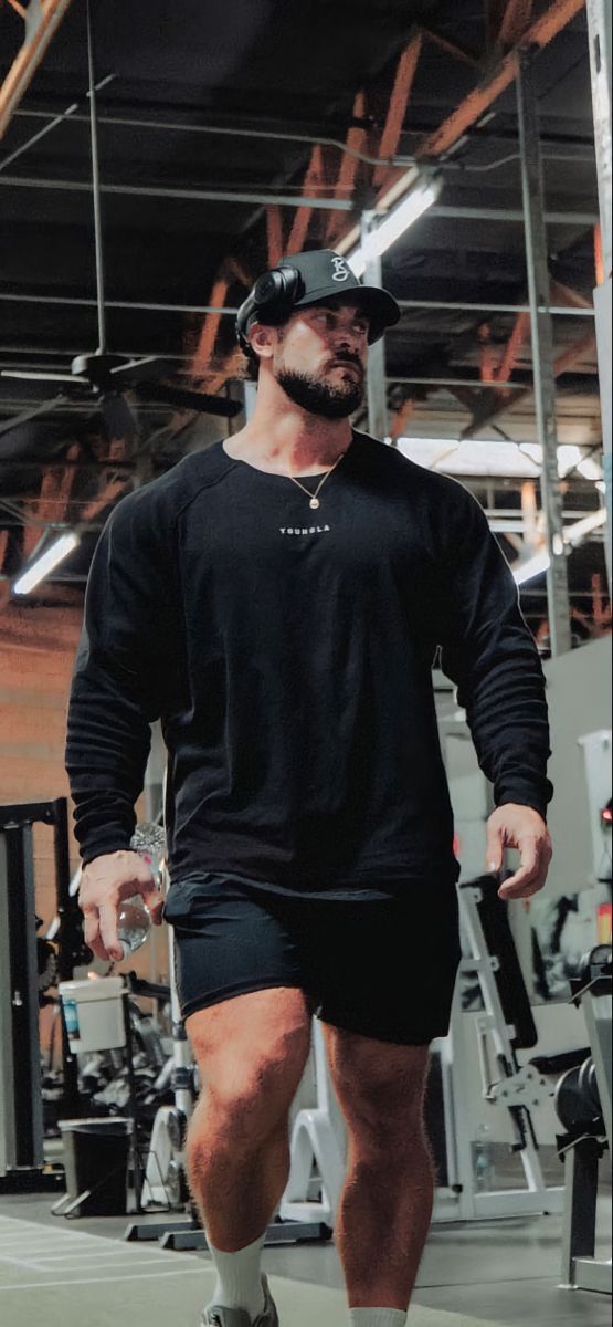 a man in black shirt and shorts walking down a gym floor