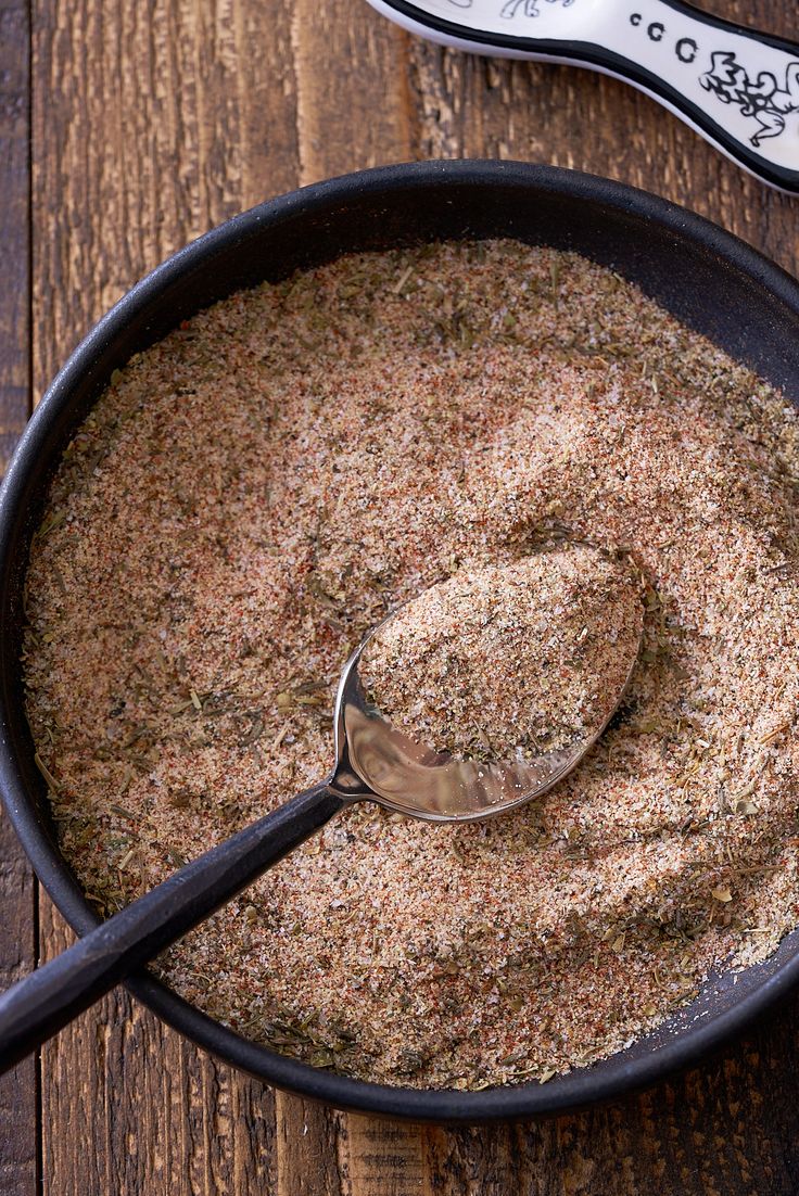 a bowl filled with seasoning next to a spoon on top of a wooden table