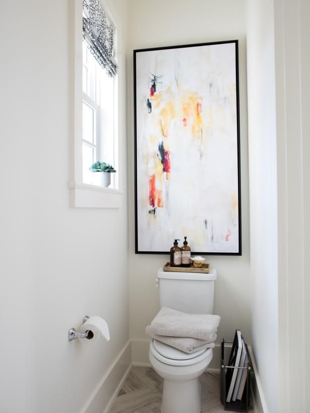 a white toilet sitting in a bathroom next to a window with a painting on the wall