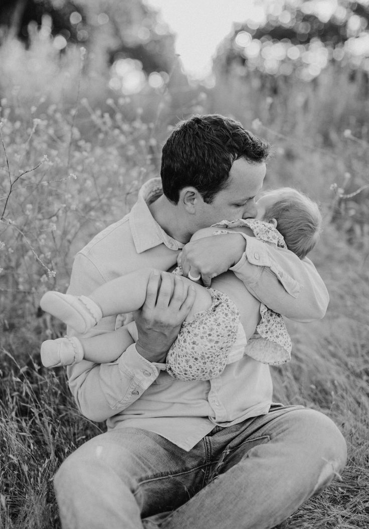 a man sitting in the grass holding a baby