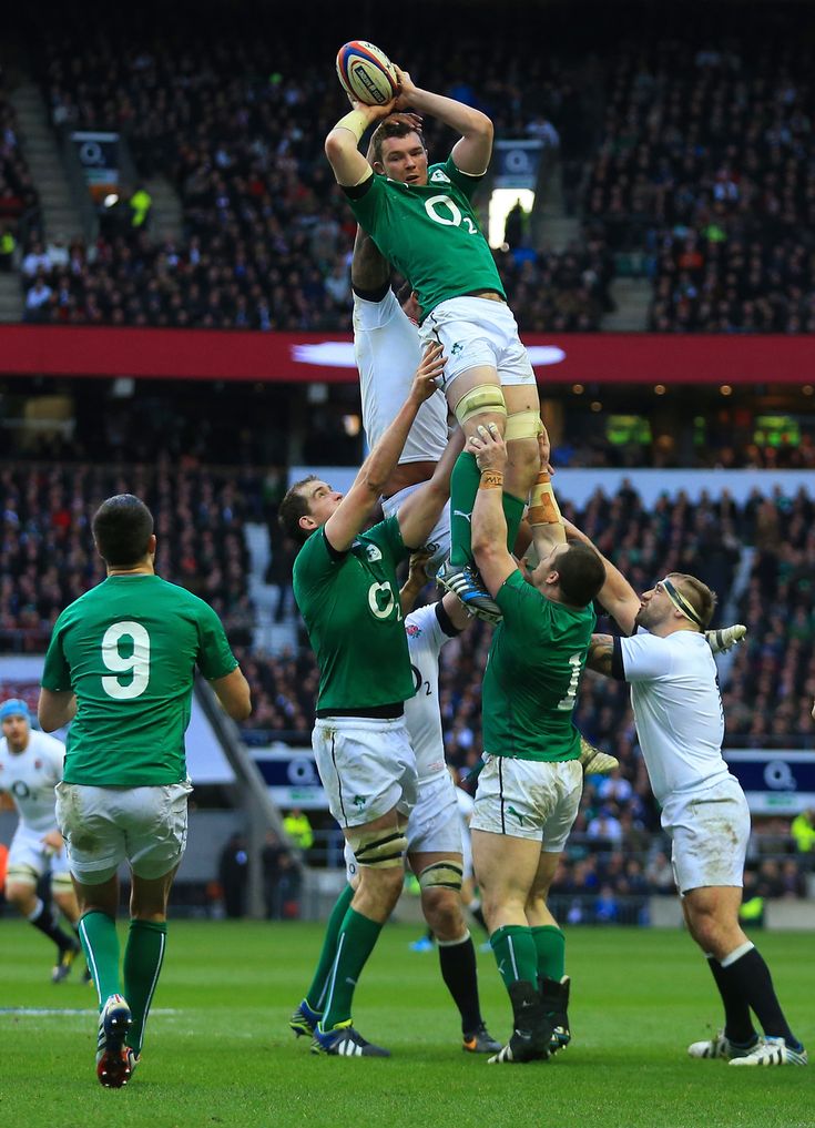 a group of men playing rugby in front of an audience at a sporting event, with one man holding the ball above his head