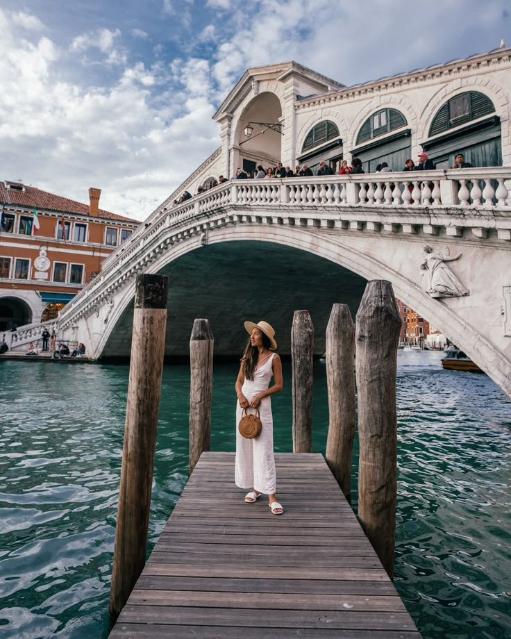 a woman standing on a pier in venice, italy with gondola bridge in the background