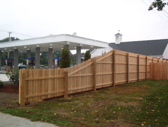 a wooden fence next to a gas station with cars parked in the lot behind it