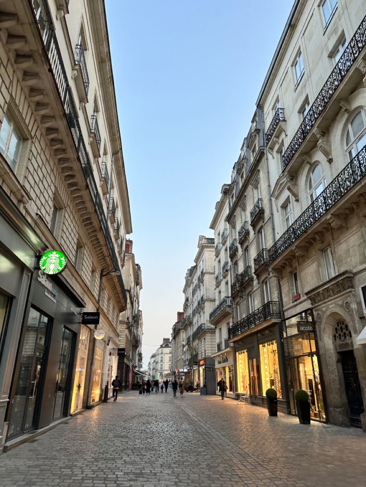 people are walking down the street in front of some tall buildings and shops on either side