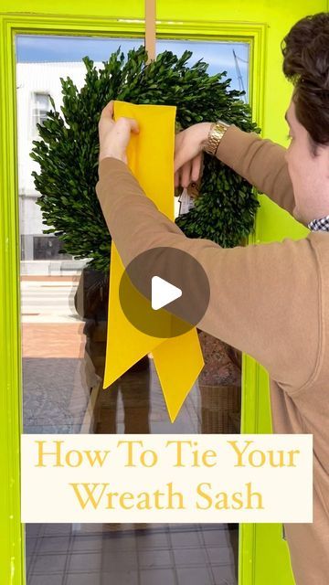 a woman placing a wreath on the front door of a house with text overlaying how to tie your wreath sash