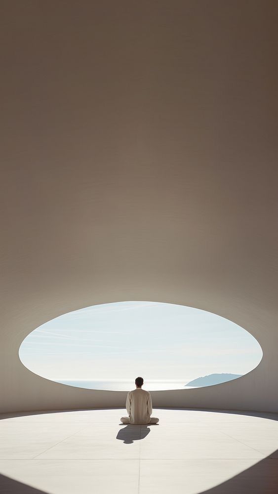 a man sitting in the middle of a room with a skylight above him and his shadow on the floor