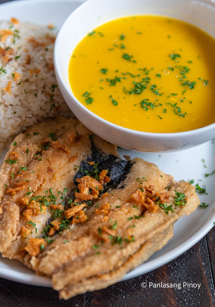 a white plate topped with food next to a bowl of soup and rice covered in parsley