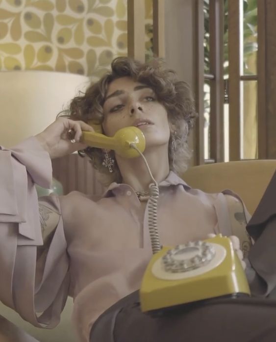 a woman sitting in a chair while talking on the phone and holding a yellow telephone to her ear