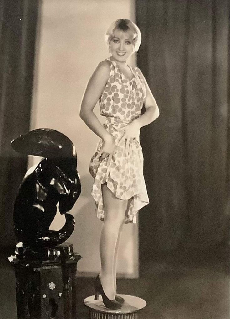 an old photo of a woman standing next to a statue