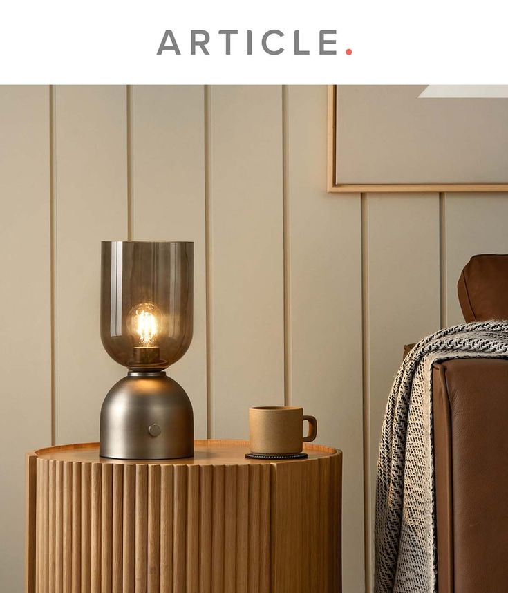 a table with a lamp on it next to a brown chair and a white wall