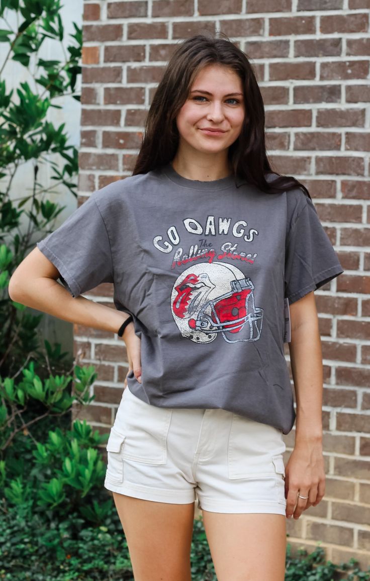 Rock ‘Em Dawgs! Nothing better than your favorite team's tee mixed with a vintage concert tee... and our Helmet Lick Thrifted Tee is just that! UGA Bulldogs meets The Rolling Stones with our oversized, slightly distressed tee in a vintage style graphic. Perfect for a cute, yet comfy look our thrifted tees pairs perfectly with biker shorts, jean shorts, or a pair of leggings and your favorite sneakers. Details: *OFFICIALLY LICENSED* Slightly Oversized Fit Vintage looking graphic Distressed detail Casual Cotton T-shirt For Game Day, Short Sleeve Tops For Football Season Streetwear, Fan Gear Graphic Print Short Sleeve T-shirt, Casual Crew Neck T-shirt For Football Season, Graphic Tee For Game Day With Short Sleeves, Retro College T-shirt For Football Season, Graphic Tee Tops For Game Day With Short Sleeves, Short Sleeve Graphic Tee For Game Day, College Graphic Tee Tops With Graphic Print